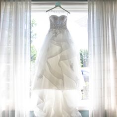 a wedding dress hanging in front of a window