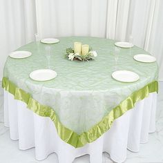 the table is set with white plates and green napkins on it, along with two votive candles