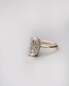 an oval shaped diamond ring on a white surface with the center stone in yellow gold