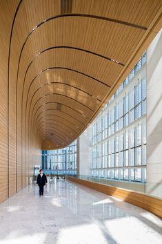 two people walking in an empty building with large windows on the walls and wood paneling