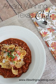 a white plate topped with chili and tortilla chips next to a napkin on top of a table