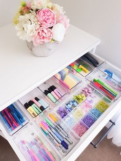 an organized drawer with pens, pencils, markers, and flowers in it on a white table