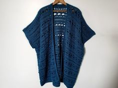 a blue crocheted cardigan hanging on a white wall next to a wooden hanger