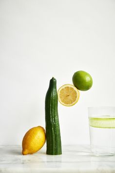 a cucumber, lemon and lime next to a glass of water