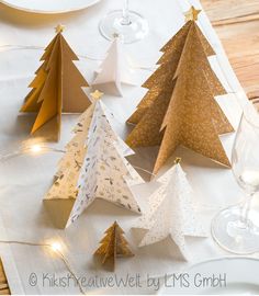 paper christmas trees sitting on top of a table next to wine glasses and silverware