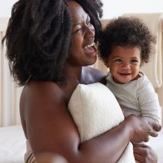 a woman holding a baby in her arms and smiling at the camera while sitting on a bed