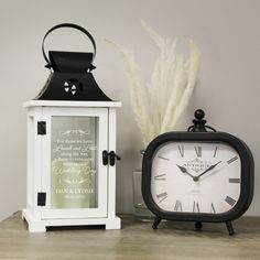 a white and black clock sitting next to a glass vase with some dry grass in it