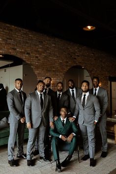 a group of men standing next to each other in front of a brick wall wearing suits and ties