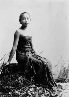 an old black and white photo of a woman sitting on the ground with grass in front of her