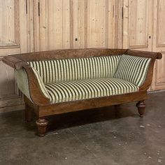 an old wooden couch with striped fabric on it's back and legs, in front of wood paneled walls