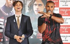 two men standing next to each other in front of a movie poster