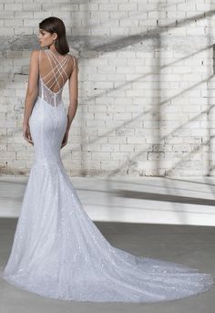 a woman in a white wedding dress standing against a brick wall with her back to the camera