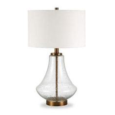 a glass table lamp with a white shade on it's side and a gold base