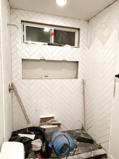 an unfinished bathroom with white tiles and no shower curtain or door, including a blue blow dryer