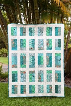 a blue and white quilt sitting on top of a lush green grass covered field next to a palm tree