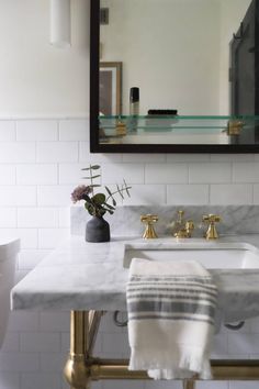 a bathroom sink with marble counter top and gold faucet, surrounded by white subway walls