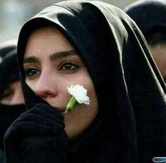 two women wearing black hoods and one is holding a white rose in her mouth