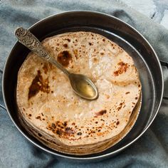 a pan filled with food on top of a blue towel next to a silver spoon