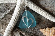 a heart shaped glass pendant sitting on top of a piece of sea glass next to a seashell