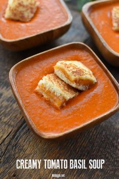 three bowls of creamy tomato basil soup with croutons in the middle, on a wooden table