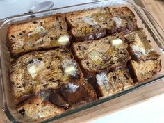 a glass dish filled with slices of bread and butter on top of a wooden table