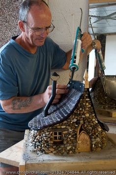 a man is making a house out of wood and rocks with a hammer on it