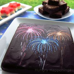 a chocolate cake with fireworks on it sitting on a table next to other desserts