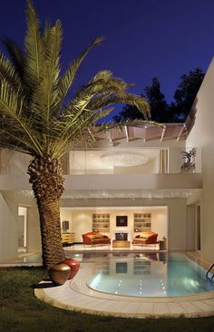 a palm tree next to a swimming pool in front of a large white house at night