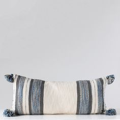 a striped pillow with pom poms on the bottom and one blue stripe down the middle