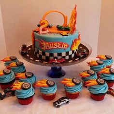 a birthday cake and cupcakes on a table with race cars around the cake