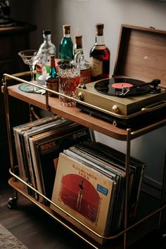 a record player sitting on top of a metal cart filled with records and liquor bottles