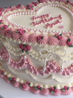 a heart shaped cake decorated with pink and white frosting, roses and pearls on top