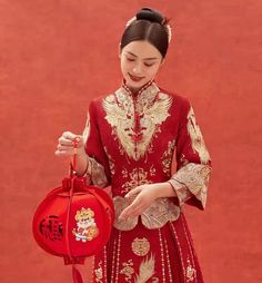 a woman in a red chinese dress holding a red bag and looking at her phone