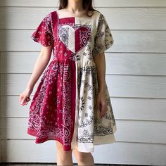 a woman standing in front of a white wall wearing a red and beige dress with paisley print