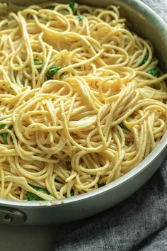 a pan filled with pasta and spinach on top of a table next to a towel