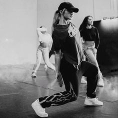 two young women are dancing on the floor in front of a wall and one is wearing a baseball cap