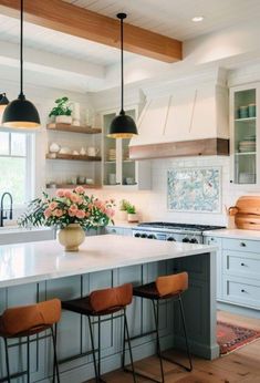 a kitchen island with three stools in front of it and flowers on the counter