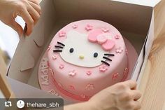 a hello kitty cake in a box with pink frosting and flowers on it, being cut