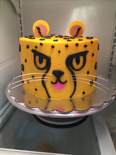 a yellow cake with black dots and a cat's face on top is sitting in the refrigerator