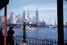 people standing on the deck of a boat in front of a large cityscape