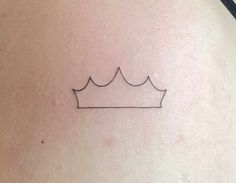 a small crown tattoo on the back of a woman's shoulder