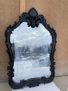 an ornate black mirror sitting on top of a white piece of paper next to a wall