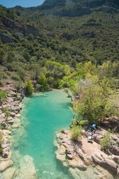 an aerial view of a river surrounded by rocks and trees with mountains in the background