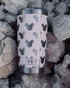 a white and black mickey mouse tumbler sitting on rocks with the word yet printed on it