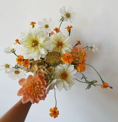 a hand holding a bouquet of flowers against a white wall with orange and white colors