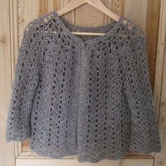 a crocheted sweater hanging on a wooden hanger in front of a door