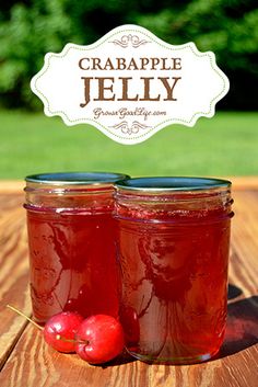 two jars filled with jelly sitting on top of a wooden table next to an apple