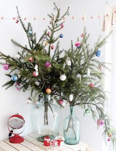 a small christmas tree in two vases on a table with ornaments hanging from it