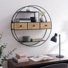 a desk with a book, lamp and vase on it in front of a wall mounted circular mirror