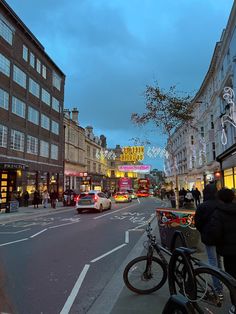 a city street filled with lots of traffic next to tall buildings and shops at dusk